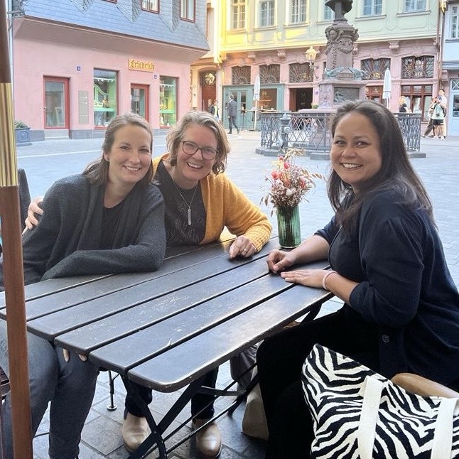 3 Frauen sitzen an einem Tisch draußen an einem Platz