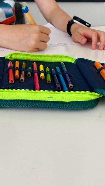 Schulmäppchen mit Stiften, Kind mit Füller im Hintergrund